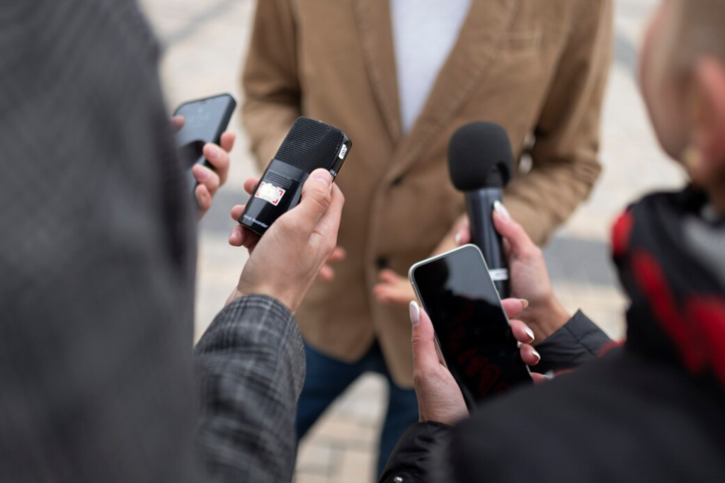 Interview scene with multiple hands holding microphones and smartphones towards a person